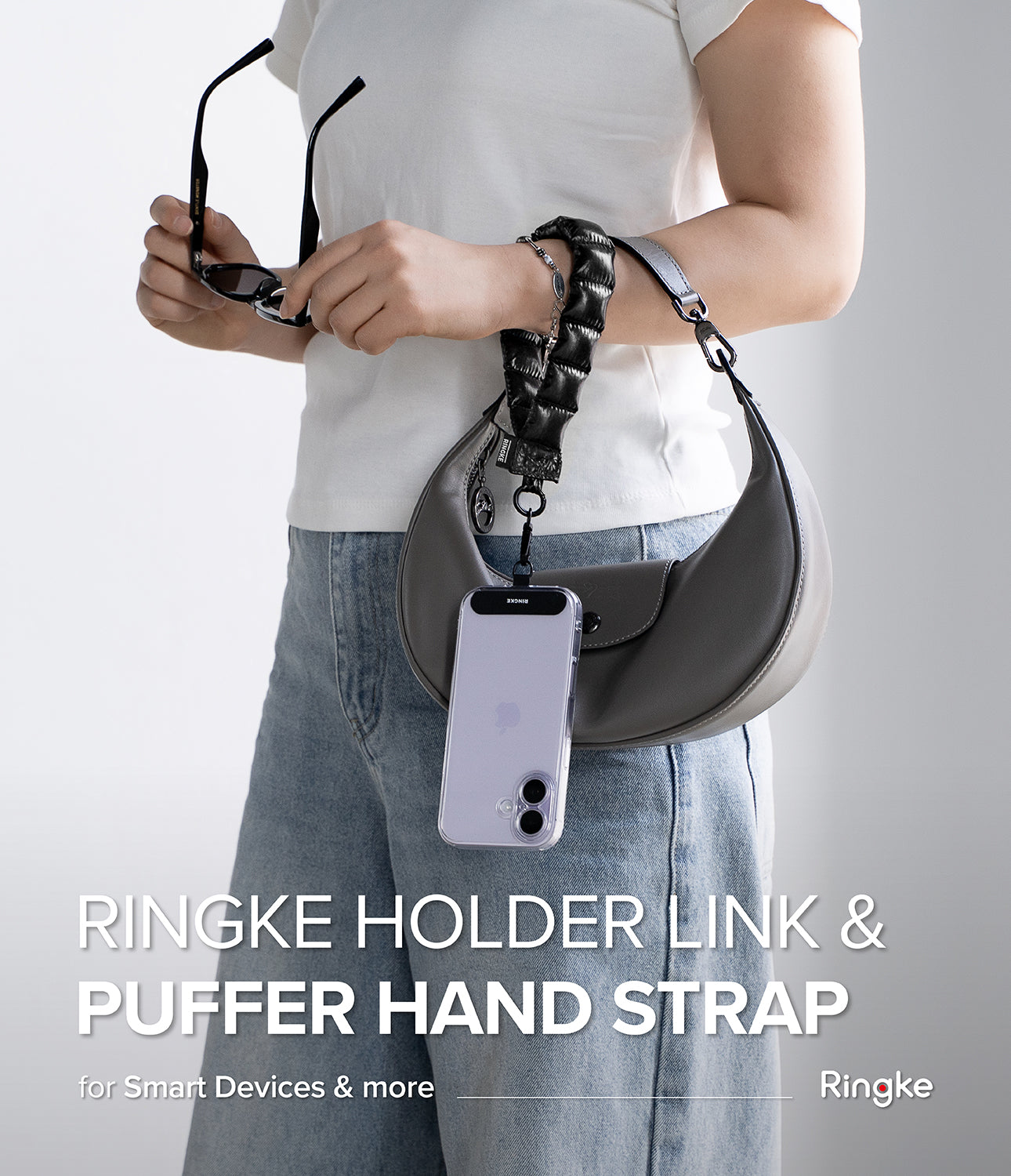 Holder Link Puffer | Hand - Person holding a gray handbag with a Ringke holder link and puffer hand strap on a light gray background