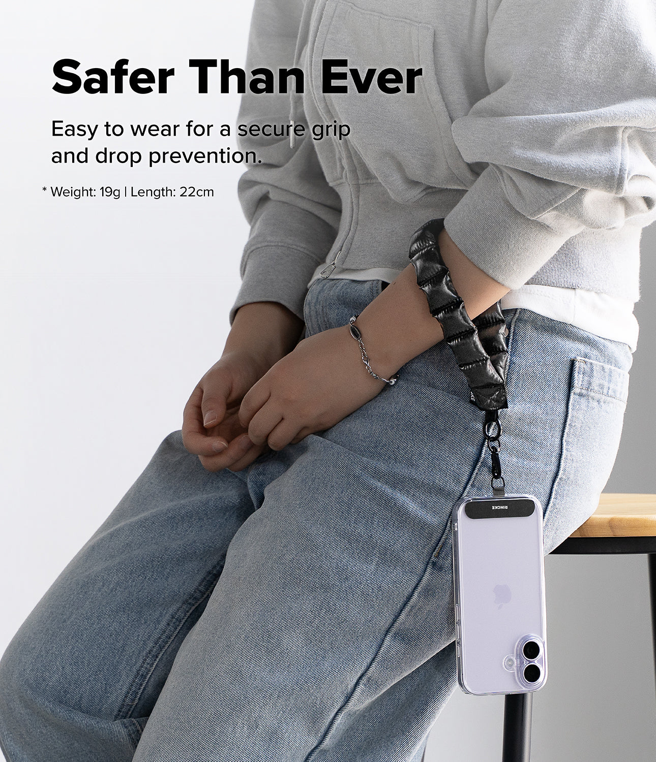 Holder Link Puffer | Hand - Person wearing a black lanyard with a phone holder, sitting on a chair.