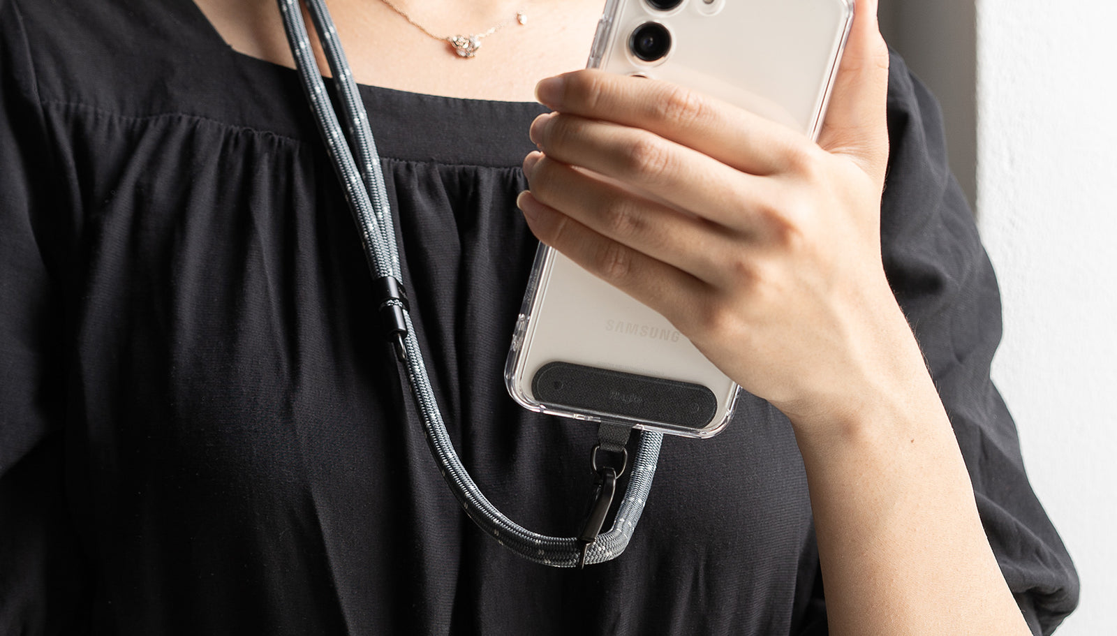 A Hand holding smartphone that attached black tether tab with strap