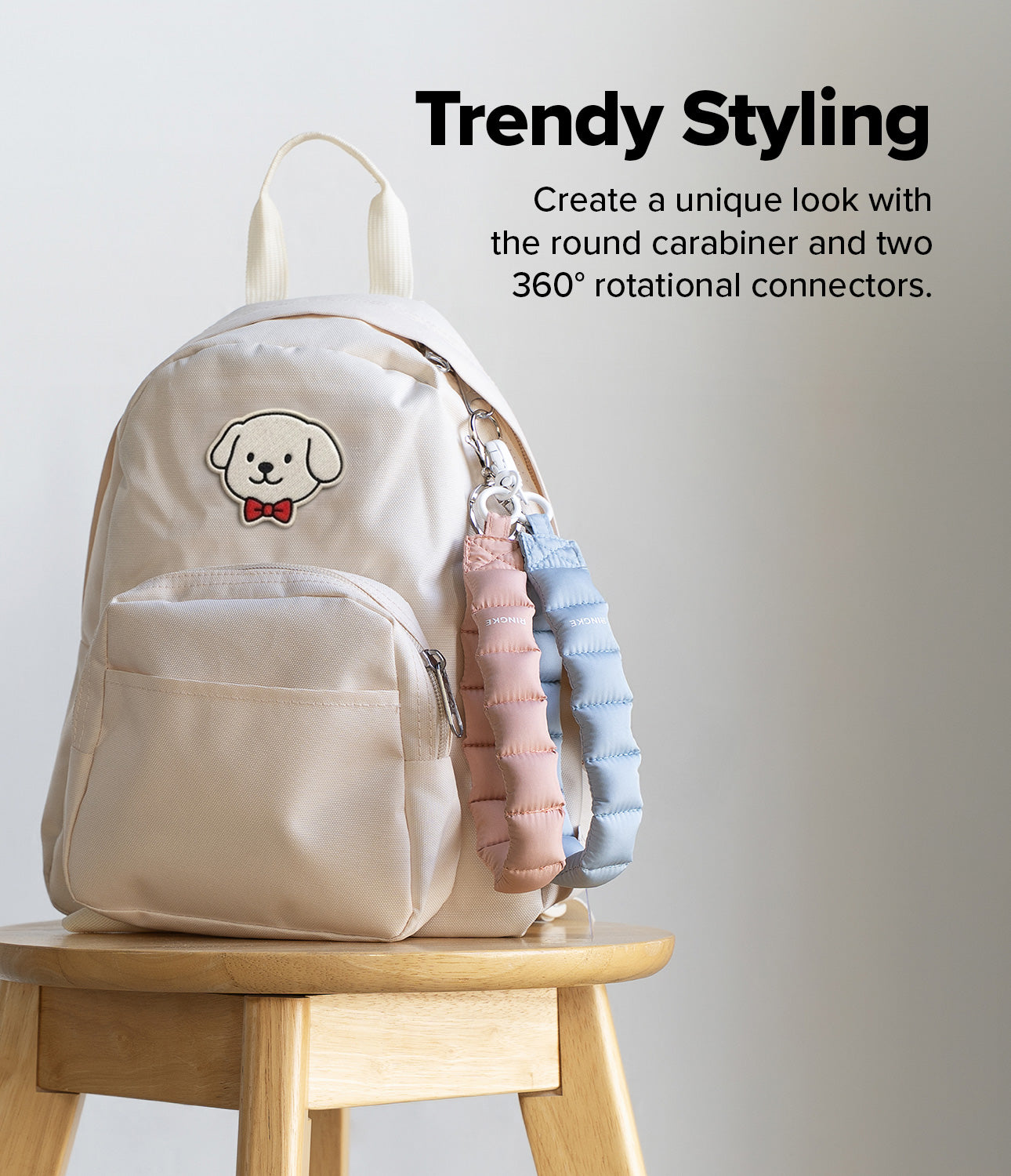 Holder Link Puffer | Hand - Cream backpack on a wooden stool with black and silver puffer straps attached by a carabiner.