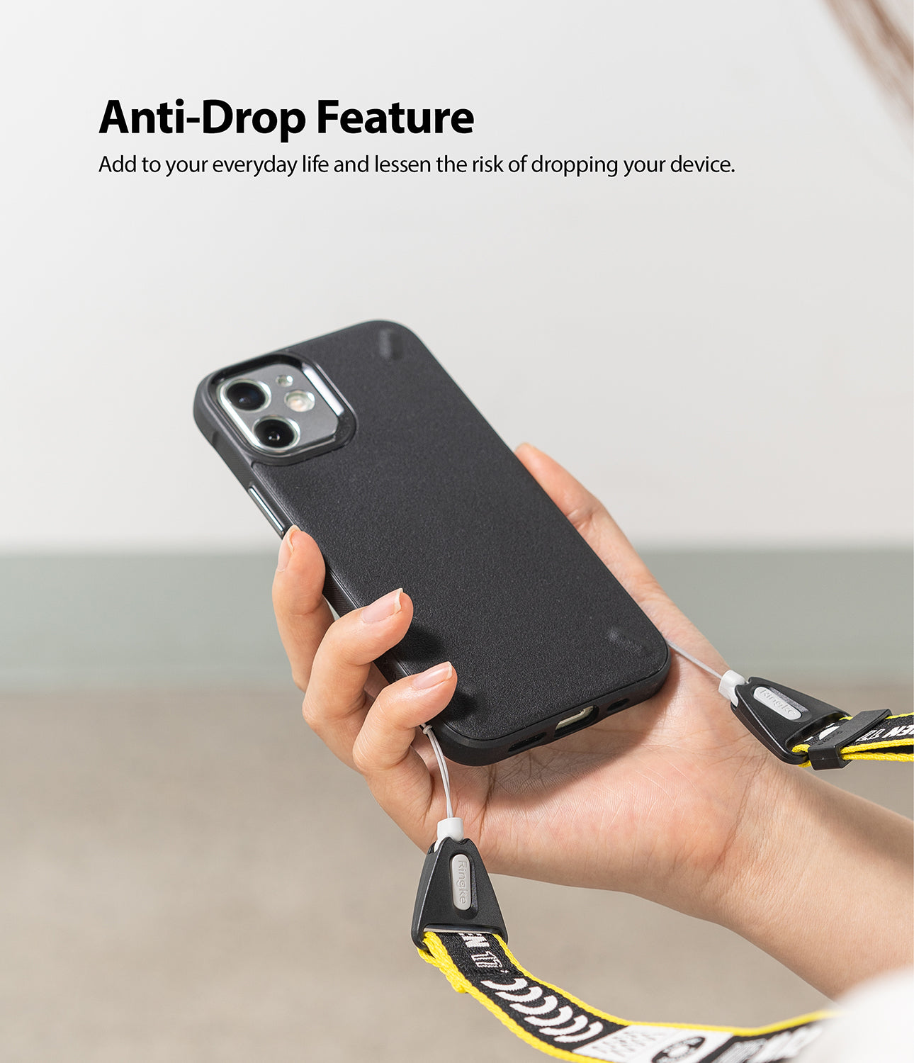 Shoulder Strap | Lettering - Hand holding a black phone case attached to a yellow and black branded shoulder strap.