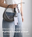 Holder Link Puffer | Finger - Person holding a gray handbag with a phone case and sunglasses, featuring Ringke holder link and puffer finger strap.