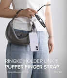 Holder Link Puffer | Finger - Person holding a gray handbag and a silver finger strap attached to a phone case, wearing a white shirt and blue jeans.
