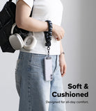 Holder Link Puffer | Hand - Person holding a black backpack with a black puffer hand strap, wearing a white shirt and blue jeans on a gray background.