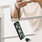 Paracord Lanyard Wrist Strap [2 Pack] - Black wrist lanyard attached to a camo phone case hanging from a person's hand.