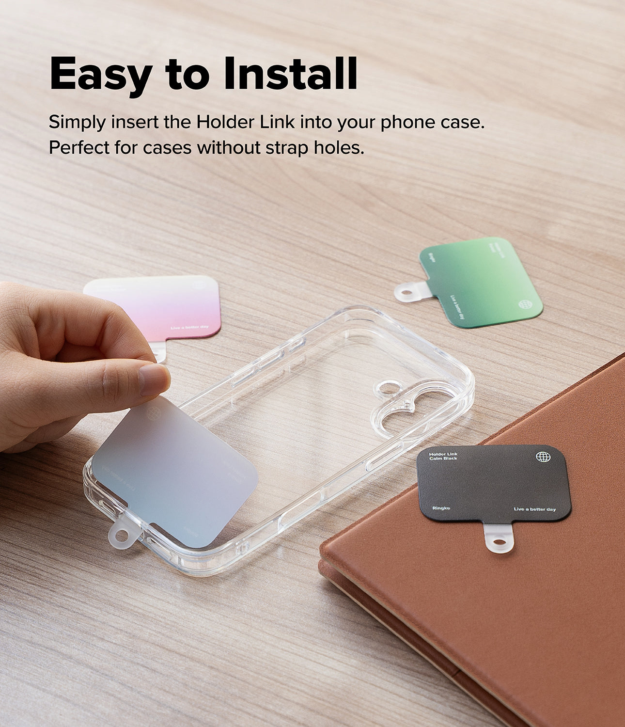 Holder Link Eyelet Keyring - Hand inserting a colorful, thin strap anchor into a clear phone case on a wooden desk.