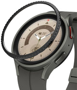 Galaxy Watch 5 Pro 45mm | Bezel Styling - Galaxy Watch 5 Pro 45mm - A black textured bezel ring hovering above a grey smartwatch with a beige analog watch face.
