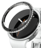 Galaxy Watch 9 / 8 40mm | Bezel Styling Premium - A close-up of a smartwatch with a white silicone strap, a black analog-style display face, and a silver-toned bezel with a textured outer ring.