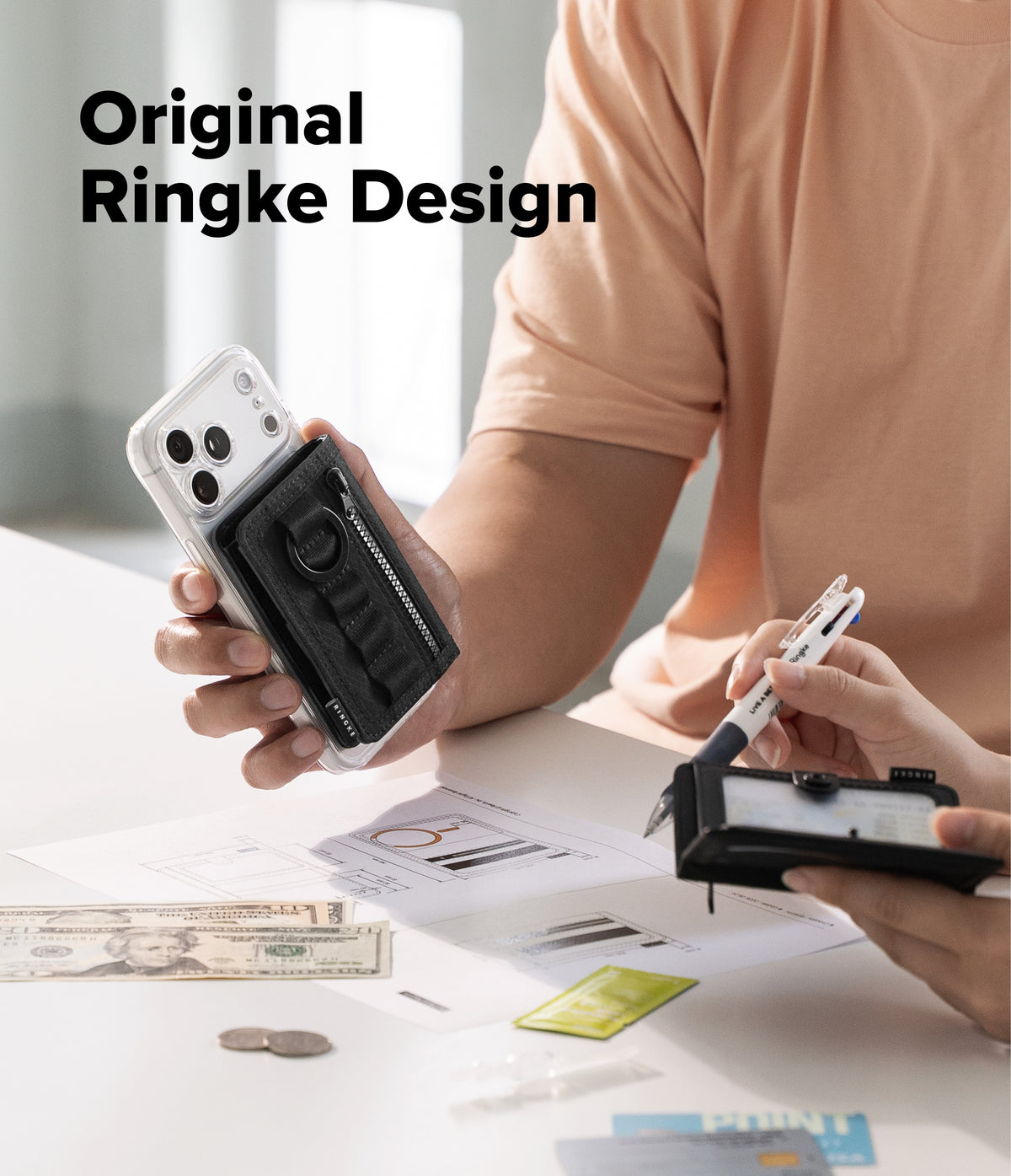 Wallet  | Tech Magnetic - A person in a peach shirt holds a black Ringke-style phone accessory with a clear case in one hand while another hand uses a pen on a small black device at a white desk. Large text reads 'Original Ringke Design' in the upper left.