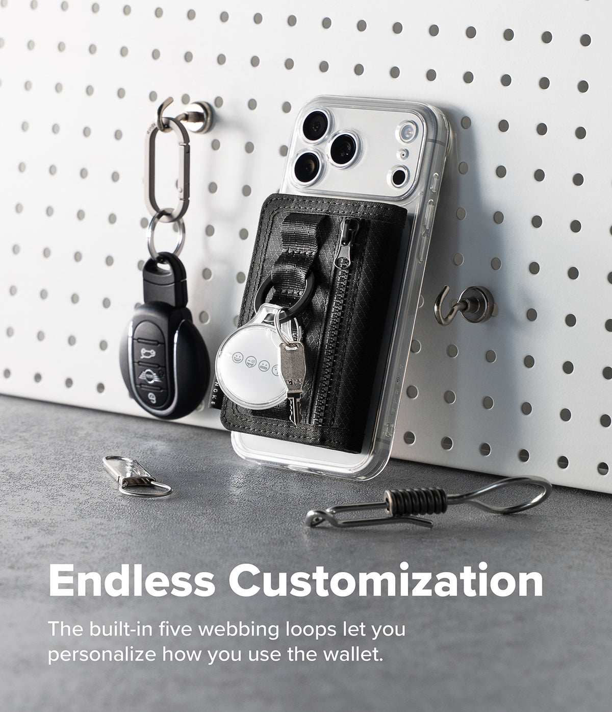 Wallet  | Tech Magnetic - A clear smartphone case with a black built-in key wallet and zipper pocket, shown leaning against a white pegboard with keys hanging nearby. Text at the bottom reads 'Endless Customization' and describes the five webbing loops for personalization.