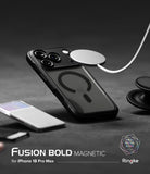 iPhone 18 Pro Max Case | Fusion Bold Magnetic Matte - A black Fusion Bold Magnetic phone case shown on an iPhone, with a white MagSafe ring attached to the back. The image is set on a dark gray textured surface with a blurred white smartphone in the foreground and a pop socket on the right.