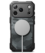 iPhone 18 Pro Max Case | Rugged Gear Magnetic - A rugged black phone case with a dark gray and black camouflage pattern back panel, featuring a large circular MagSafe-compatible magnetic ring on the back and a white charging cable extending from it, shown on a white background.