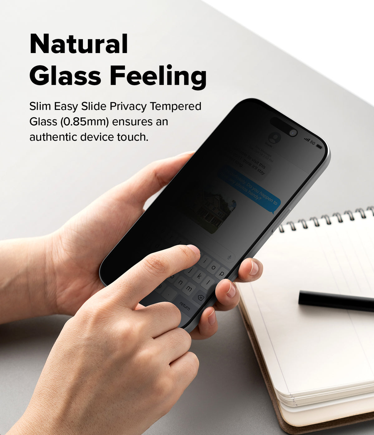 iPhone 18 Pro Screen Protector | Easy Slide Privacy Tempered Glass - A person holds a smartphone with a dark privacy screen protector in both hands over a light gray desk, with a notebook and pen nearby. Text on the left reads 'Natural Glass Feeling' and describes slim easy slide privacy tempered glass.