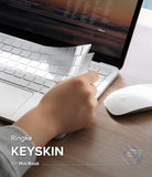 MacBook Neo | Keyskin - A hand peels back a transparent protective keyboard skin from a silver MacBook keyboard, with a white mouse on a wooden desk. Text on the image reads 'Ringke KEYSKIN for MacBook'.