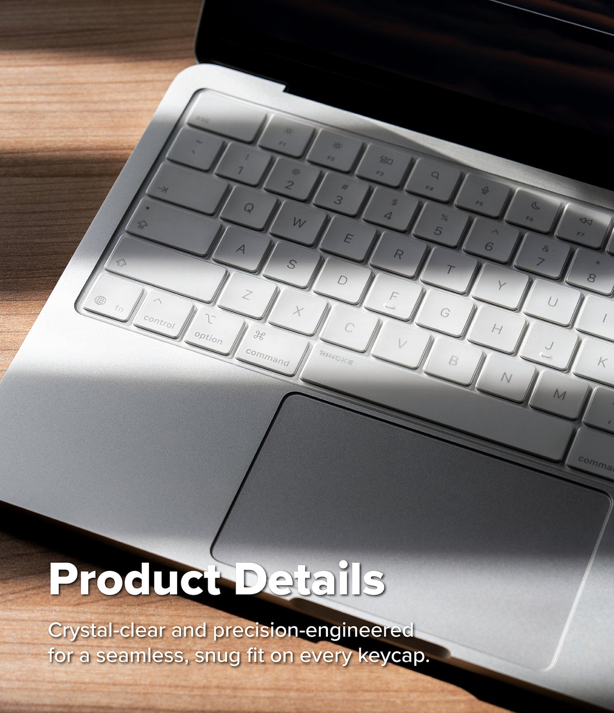 MacBook Neo | Keyskin - Close-up of a silver laptop keyboard with a translucent clear keycap cover, resting on a wooden surface with soft sunlight and shadow. White text at the bottom reads 'Product Details' with descriptive copy about crystal-clear and precision-engineered keycaps.