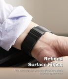 Galaxy Watch Ultra 2 / 1 | Metal One Mesh - A close-up of a black metal D-buckle watch with a black mesh strap worn on a wrist, with a white shirt cuff visible. Text overlays read 'Refined Surface Finish' and 'Fine hairline polish gives the D-buckle a sleek, luxurious appearance.