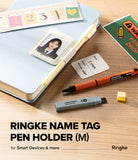 Pen Holder | Name Tag (2P) - A Ringke name tag pen holder in size M, shown in a styled flat-lay on a wooden desk alongside a light blue notebook, an orange pen, a gray highlighter, and a sample photo insert.