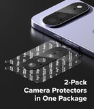 Google Pixel 11 Camera Protector | Camera Full Cover Tempered Glass (2 Pack) - Two-pack of camera protectors shown with a smartphone on a dark reflective surface. The protectors are black circular lens covers with white protective tape printed on the back.