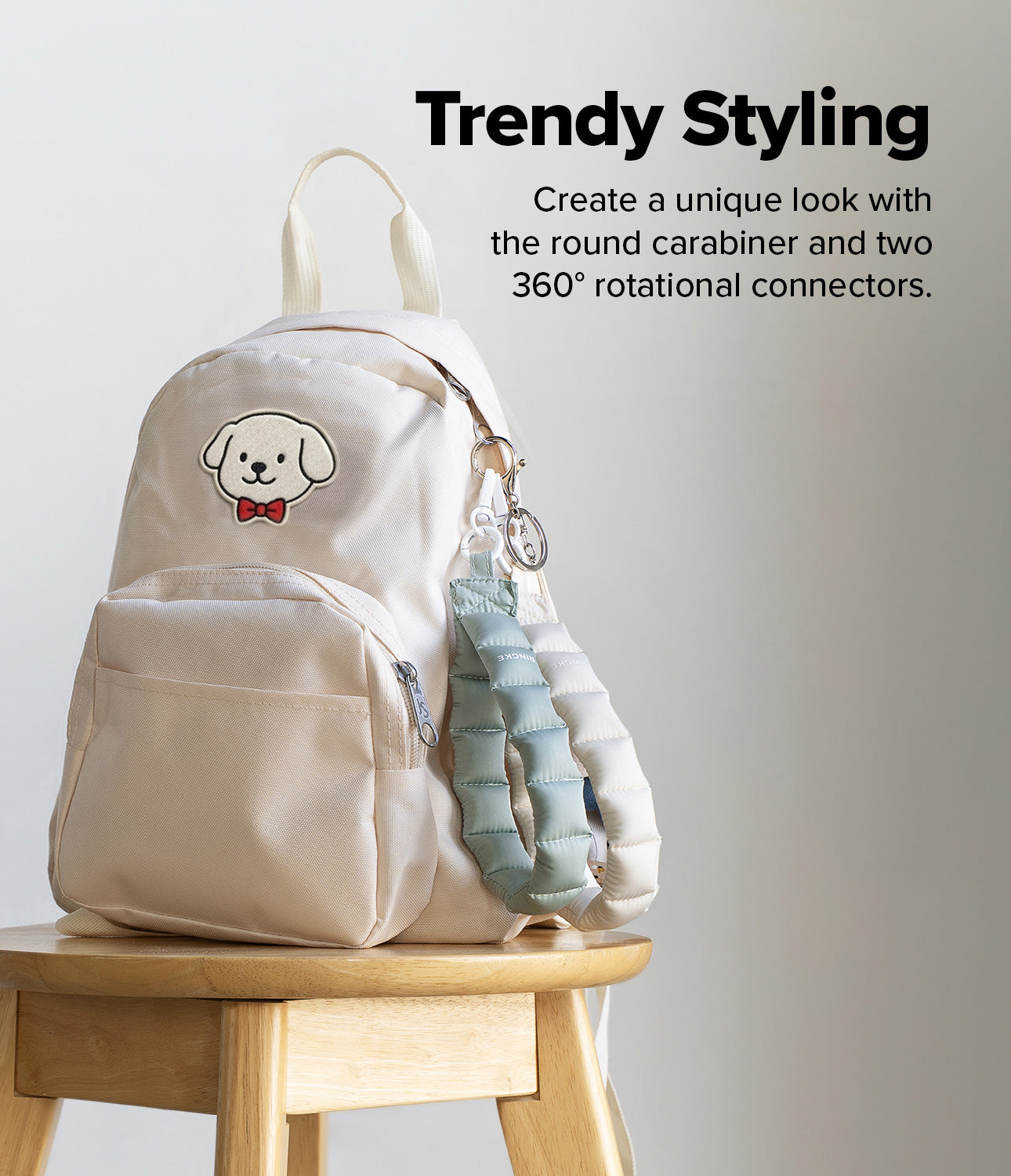 Holder Link Puffer | Hand - Cream backpack on a wooden stool with black and silver puffer straps attached by a carabiner.