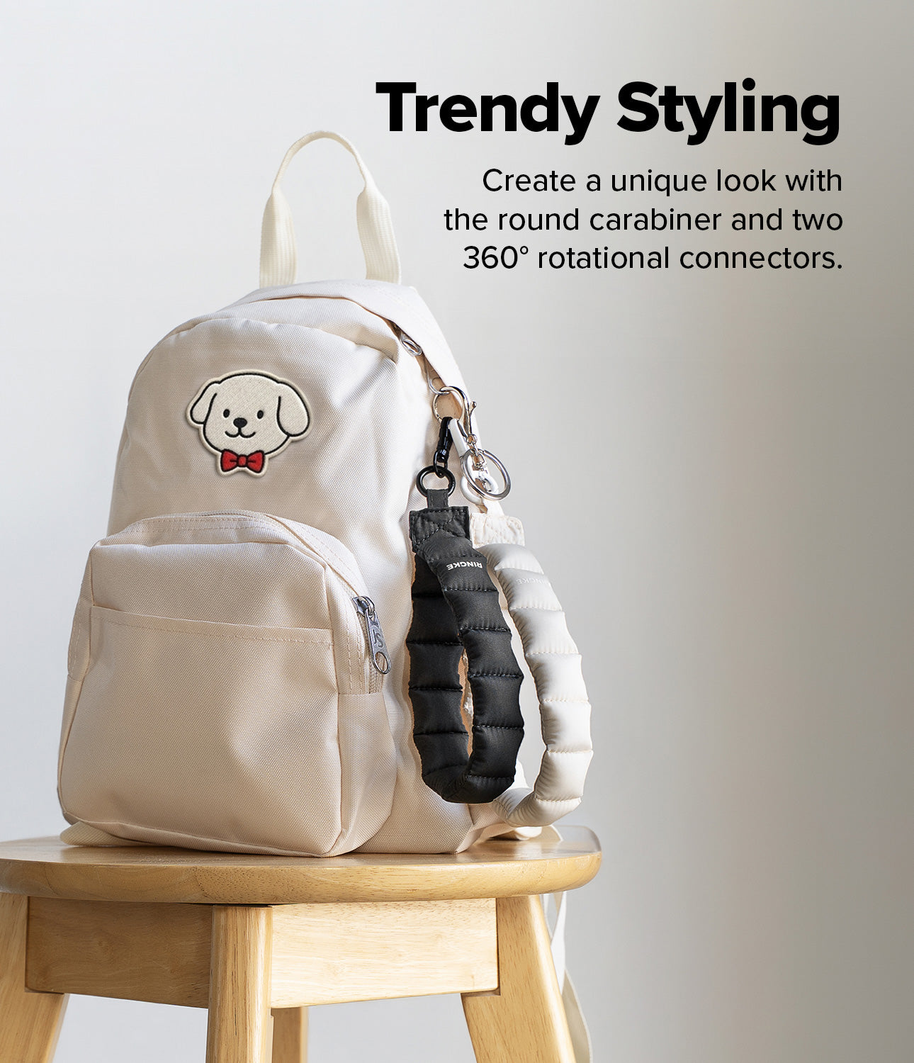 Holder Link Puffer | Hand - Cream backpack on a wooden stool with black and silver puffer straps attached by a carabiner.