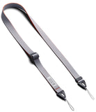 Design Shoulder Strap - A smartphone in a clear case attached to a grey adjustable shoulder strap resting on an open book.