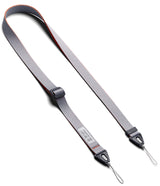 Design Shoulder Strap - A smartphone in a clear case attached to a grey adjustable shoulder strap resting on an open book.