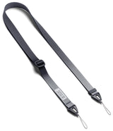 Design Shoulder Strap - A clear phone case with a black shoulder strap resting on an open book with other colorful straps.