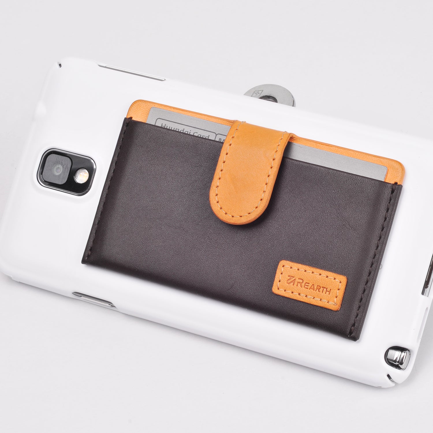 Ringke® Leather ID / Card Holder, 3M Adhesive Stick On Mini Wallet Attachment for All Phone Devices - Ringke® Leather ID / Card Holder - Brown and tan leather adhesive card wallet attached to the back of a white smartphone.