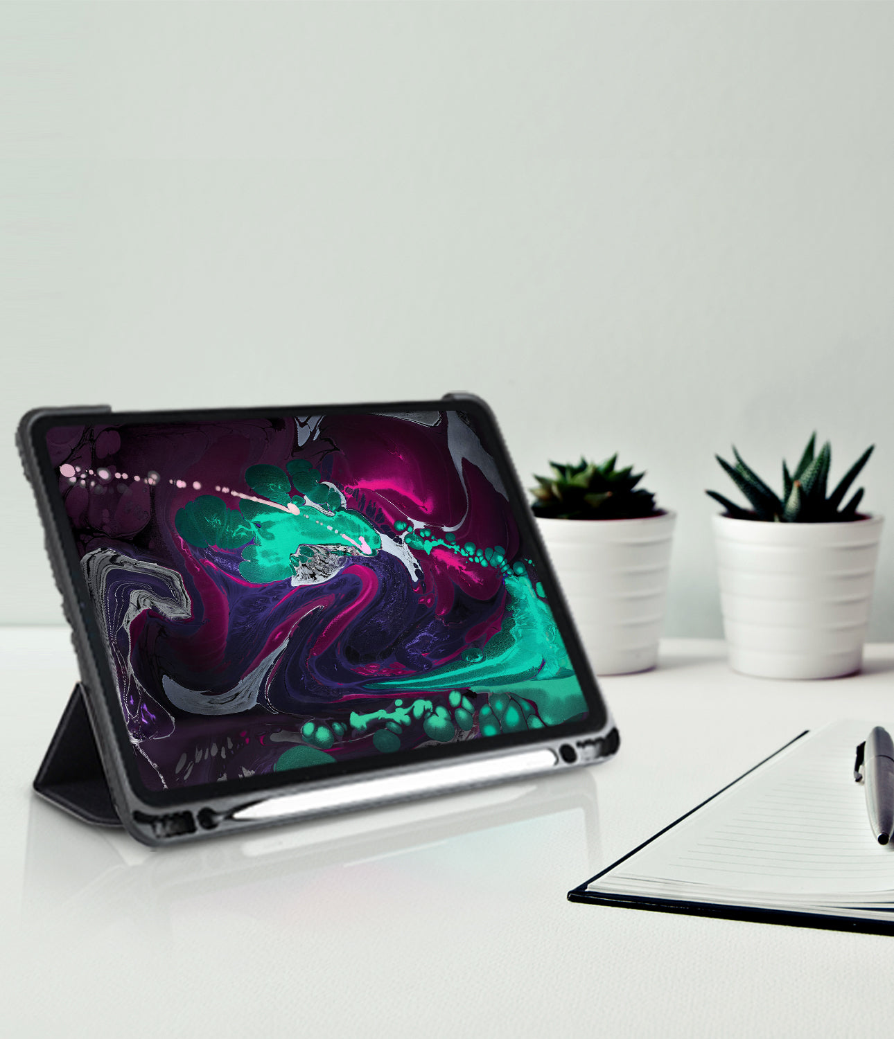 Smart Cover Apple Pencil Stand | iPad - A tablet in a black protective case with a kickstand, displayed on a white desk with a notebook, pen, and small potted plants in the background.