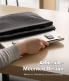 Step-Fit Mini Stand - A person's hand is shown attaching a silver laptop to a black adhesive laptop sleeve on a light wood desk. The text overlay reads 'Adhesive-Mounted Design' and 'Made for effortless carry and storage.