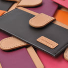 Ringke® Leather ID / Card Holder, 3M Adhesive Stick On Mini Wallet Attachment for All Phone Devices - Ringke® Leather ID / Card Holder - A black leather card holder with a tan strap and Rearth logo, stacked over colorful wallets.